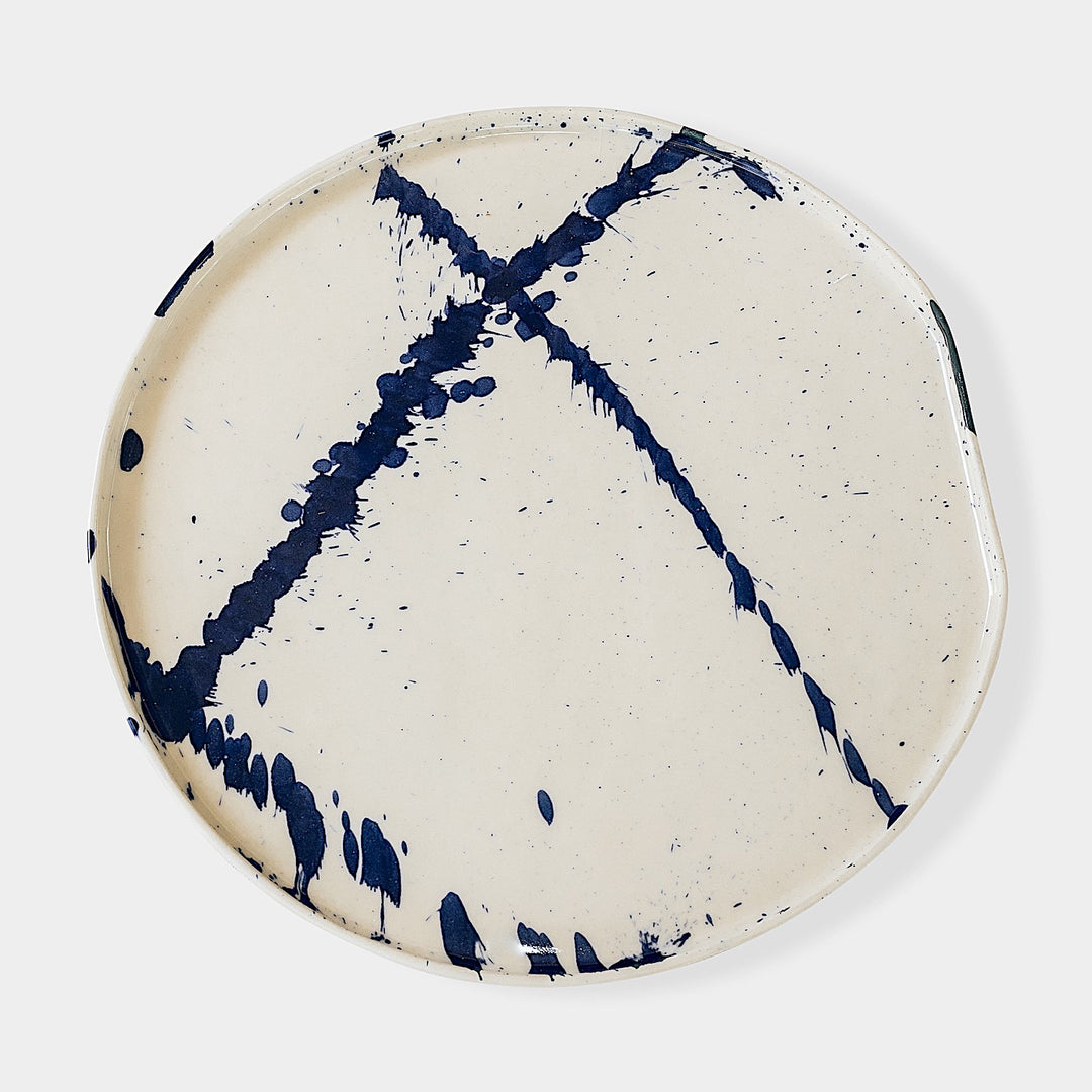 The Earl Home PLATES feature a round ceramic design with a white base and two intersecting dark blue splatter patterns. They are both dishwasher and microwave safe.