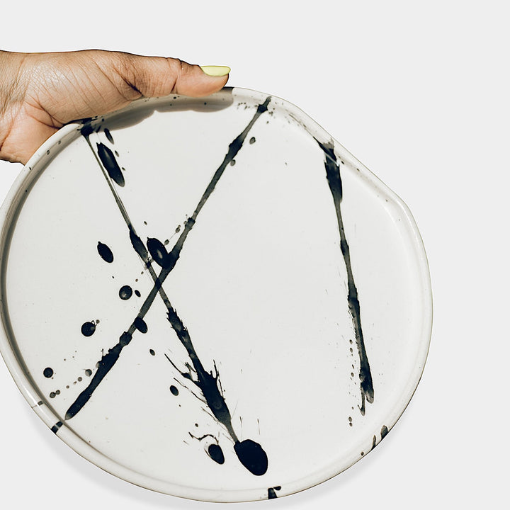 The Earl Home PLATES feature a round ceramic design with a white base and two intersecting dark blue splatter patterns. They are both dishwasher and microwave safe.