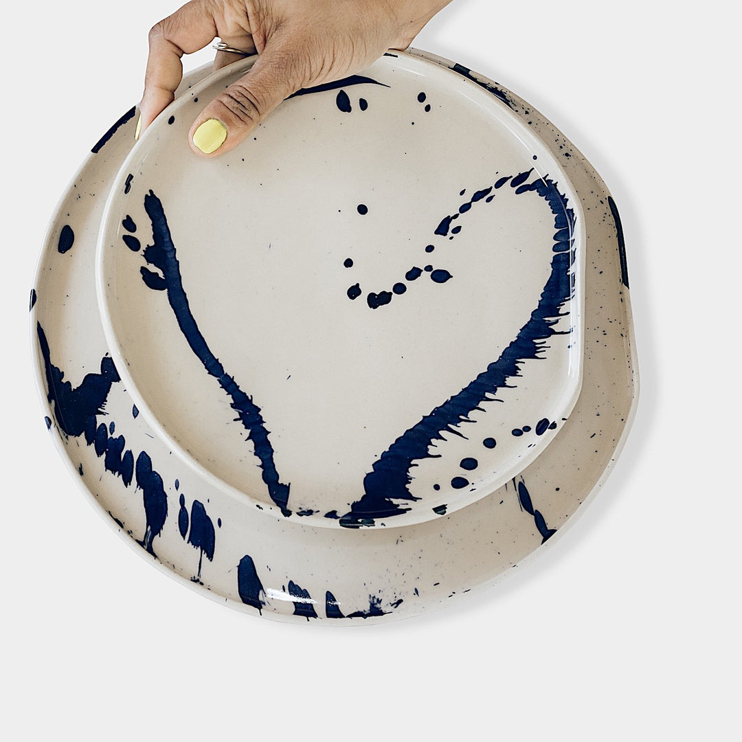 The Earl Home PLATES feature a round ceramic design with a white base and two intersecting dark blue splatter patterns. They are both dishwasher and microwave safe.