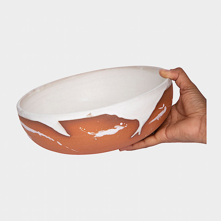 The Earl Home SERVING Bowl is a hand-thrown ceramic piece featuring a white interior and terracotta exterior with elegant swirl patterns. It is dishwasher and microwave safe.