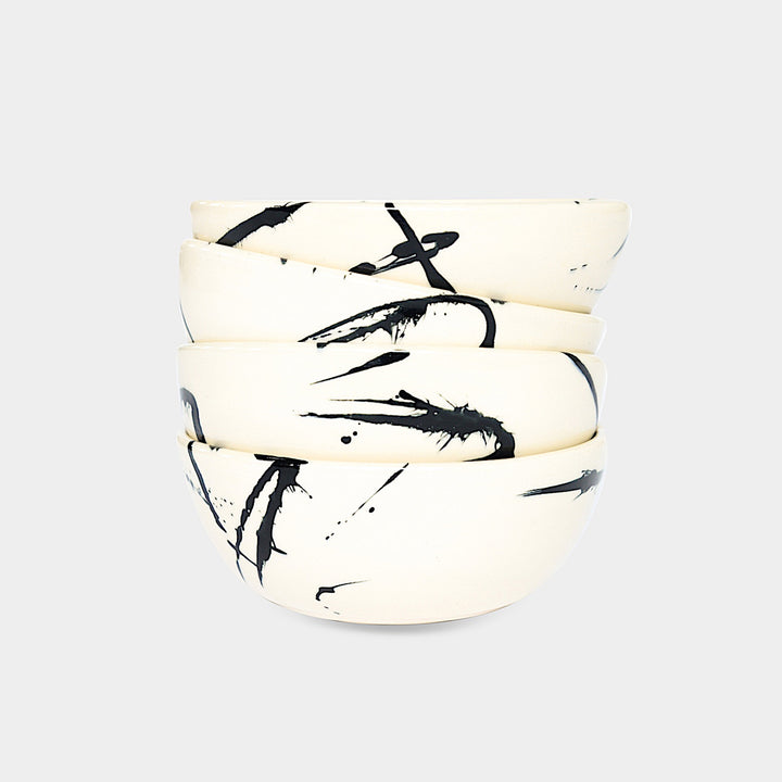 The Earl Home CEREAL Bowl features a white ceramic design with a black abstract splatter, set against a plain background. Microwave and dishwasher safe, it blends artistry and functionality for everyday use.