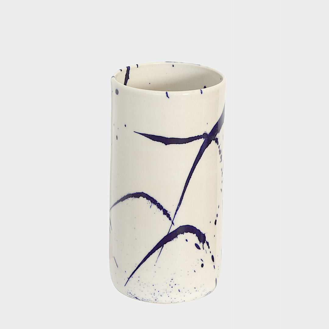 The TALL Cylinder cup by Earl Home features meticulous artistry with its hand-thrown white ceramic and abstract blue brushstrokes against a plain white background.