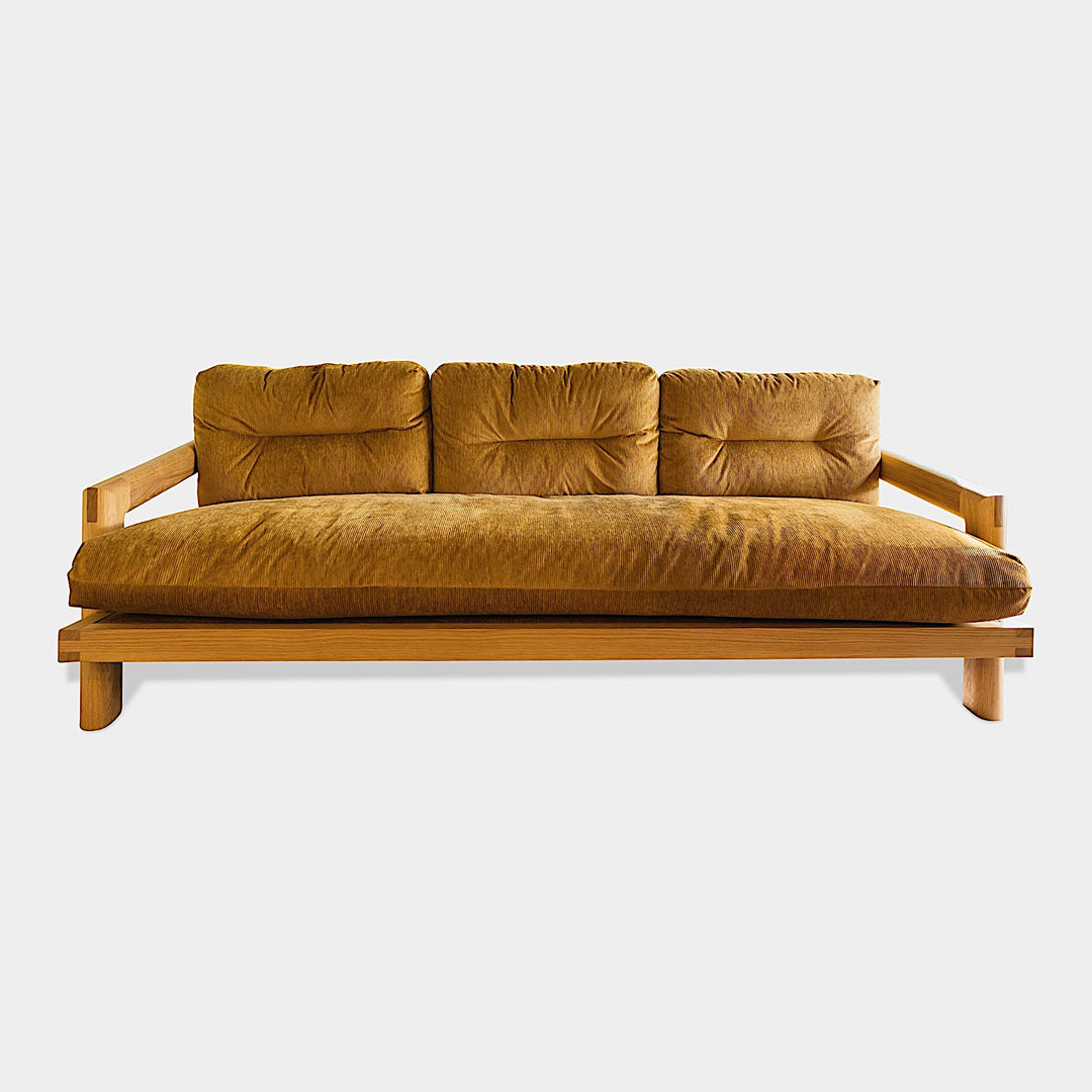 The White Oak TAMBU Sofa by Earl Home is a modern classic with a minimalist wooden frame of elegant White Oak, enhanced by three mustard cushions set against a white backdrop.