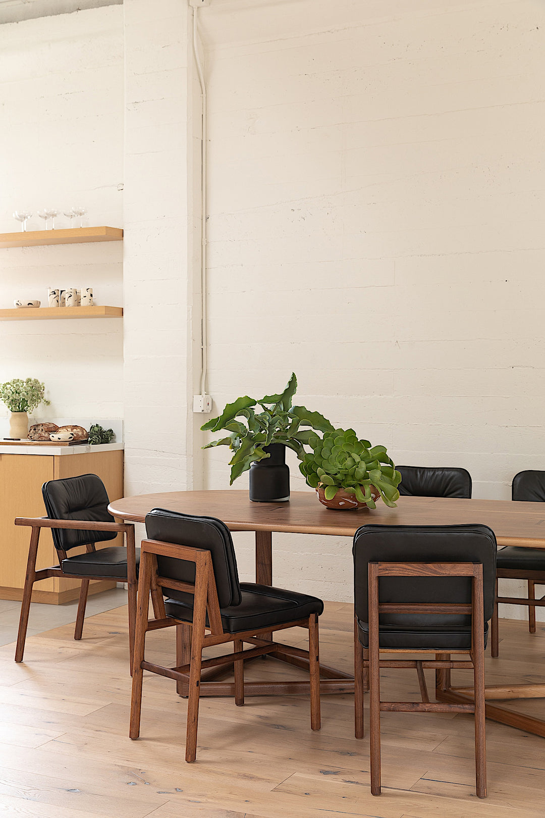 The WOLF Dining Table by Earl Home features a long, oval solid wood design with two geometric rectangular legs, elegantly displayed on a white background to highlight the beauty of unique wood furniture.