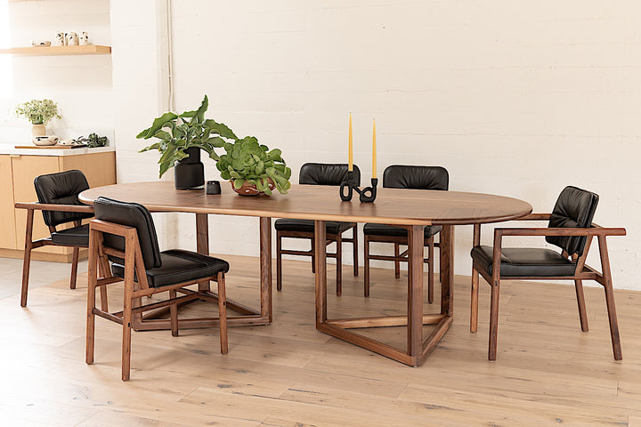 The WOLF Dining Table by Earl Home features a long, oval solid wood design with two geometric rectangular legs, elegantly displayed on a white background to highlight the beauty of unique wood furniture.