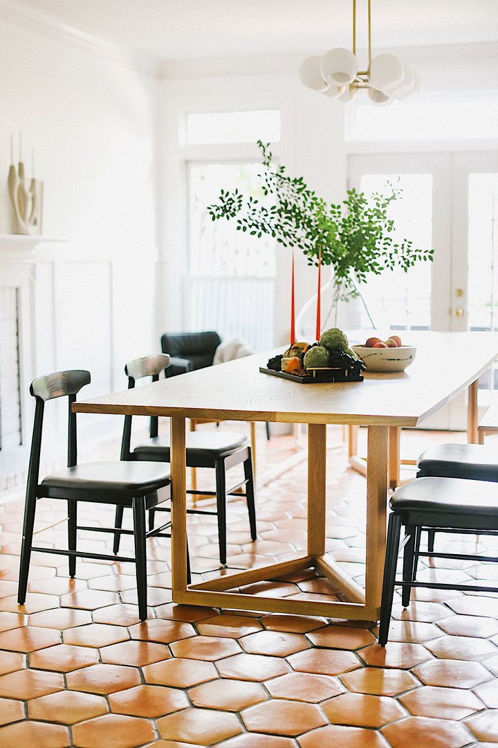 The WOLF Dining Table by Earl Home features a long, oval solid wood design with two geometric rectangular legs, elegantly displayed on a white background to highlight the beauty of unique wood furniture.