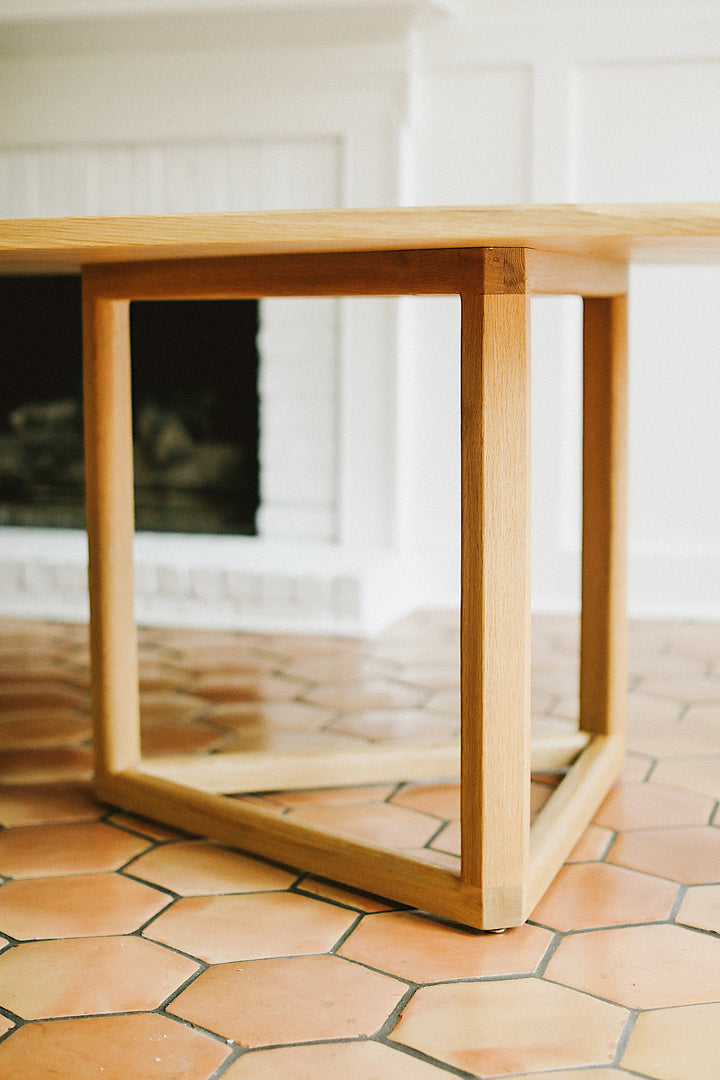 The WOLF Dining Table by Earl Home features a long, oval solid wood design with two geometric rectangular legs, elegantly displayed on a white background to highlight the beauty of unique wood furniture.