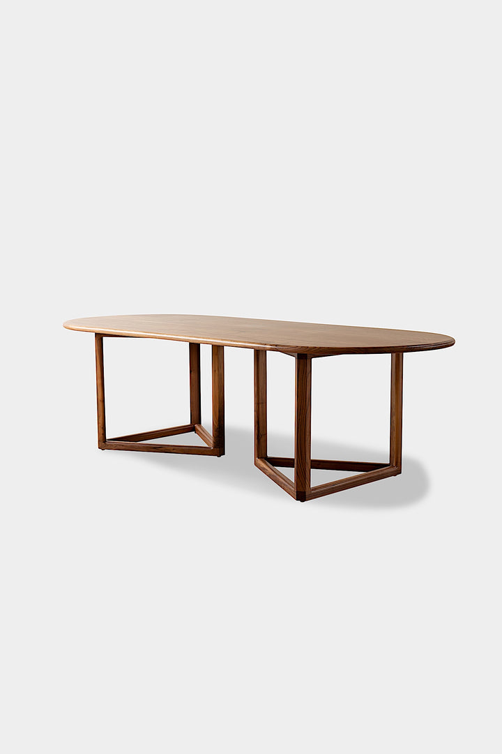 The WOLF Dining Table by Earl Home features a long, oval solid wood design with two geometric rectangular legs, elegantly displayed on a white background to highlight the beauty of unique wood furniture.