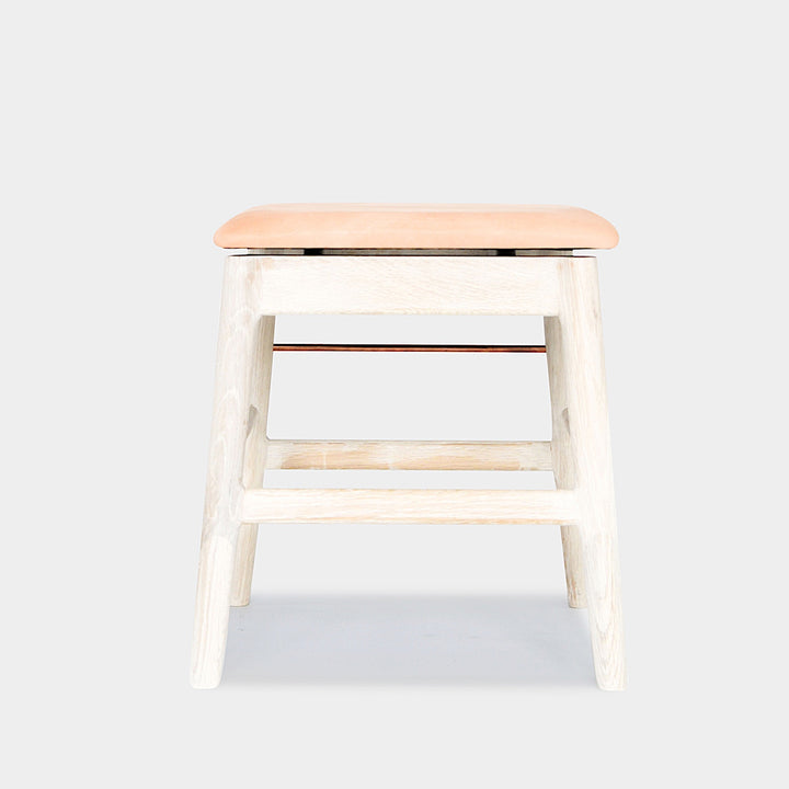 The WOOD Low Stool by Earl Home features a handmade wooden design, a custom upholstered black cushioned seat, and a brass footrest bar, all set against a plain background.