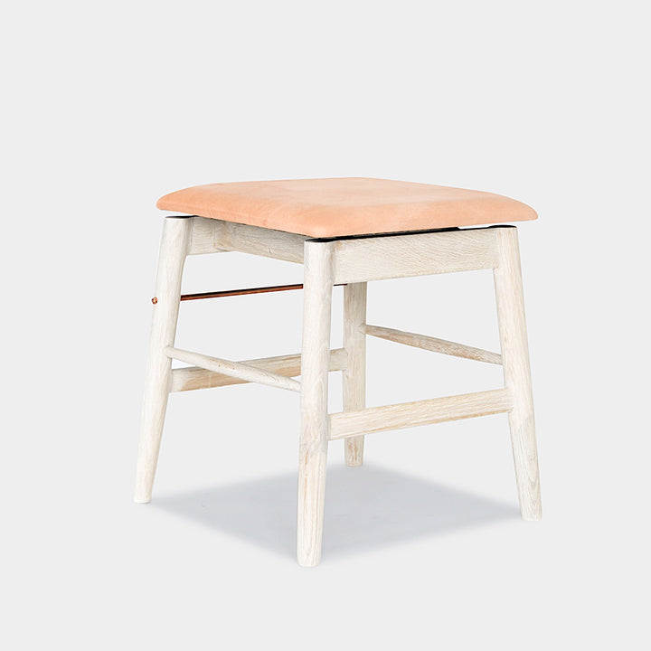 The WOOD Low Stool by Earl Home features a handmade wooden design, a custom upholstered black cushioned seat, and a brass footrest bar, all set against a plain background.