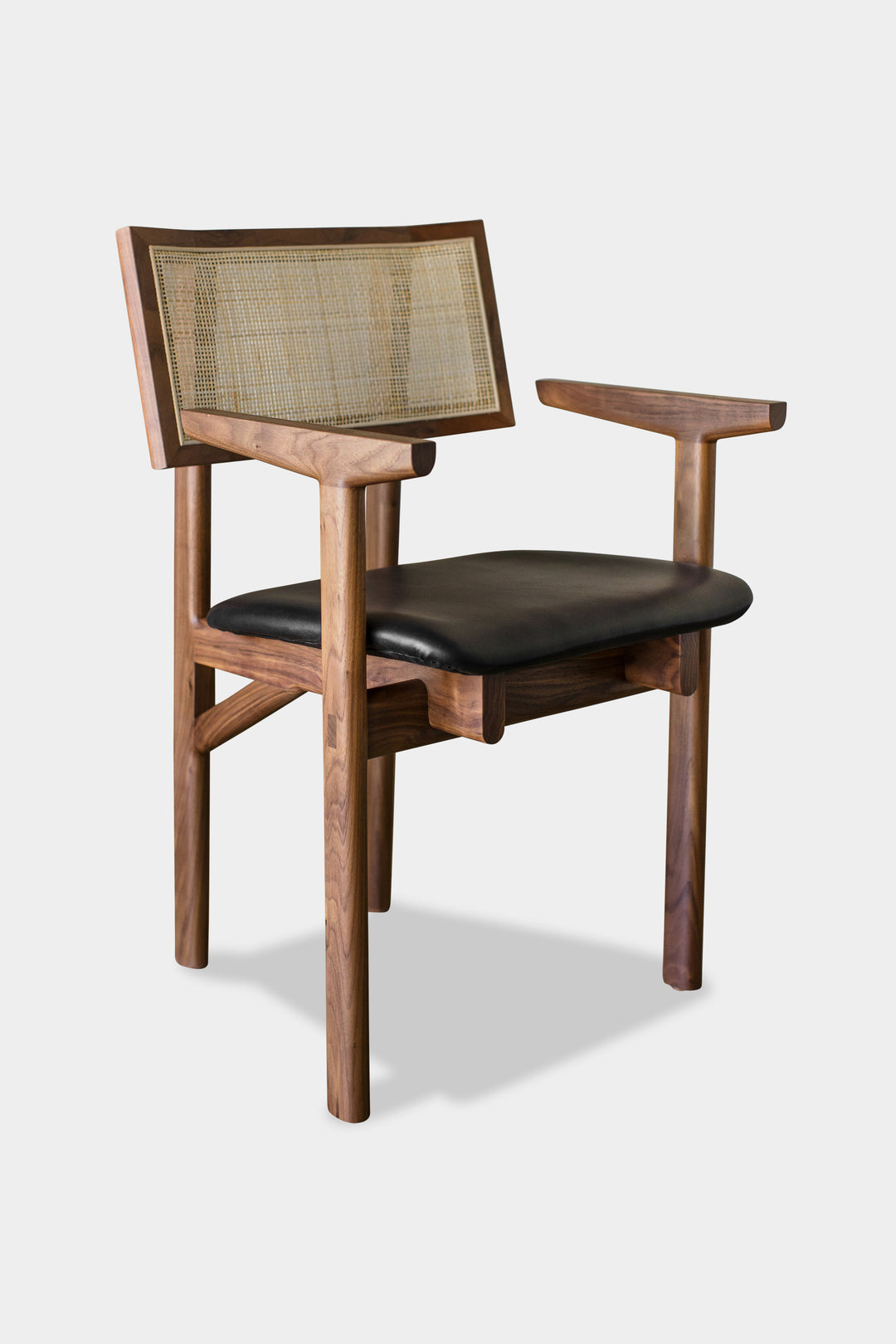 The KUNAI Captain Chair by Earl Home is a solid wood dining chair with armrests, a woven rattan backrest, and a custom upholstered black cushioned seat, all enhanced by intricately hand-shaped legs.