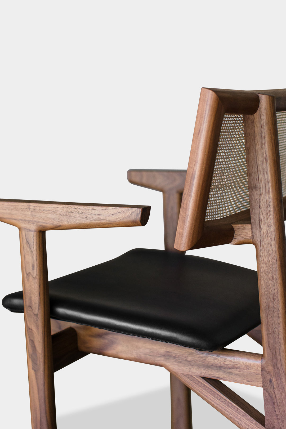 The KUNAI Captain Chair by Earl Home is a solid wood dining chair with armrests, a woven rattan backrest, and a custom upholstered black cushioned seat, all enhanced by intricately hand-shaped legs.