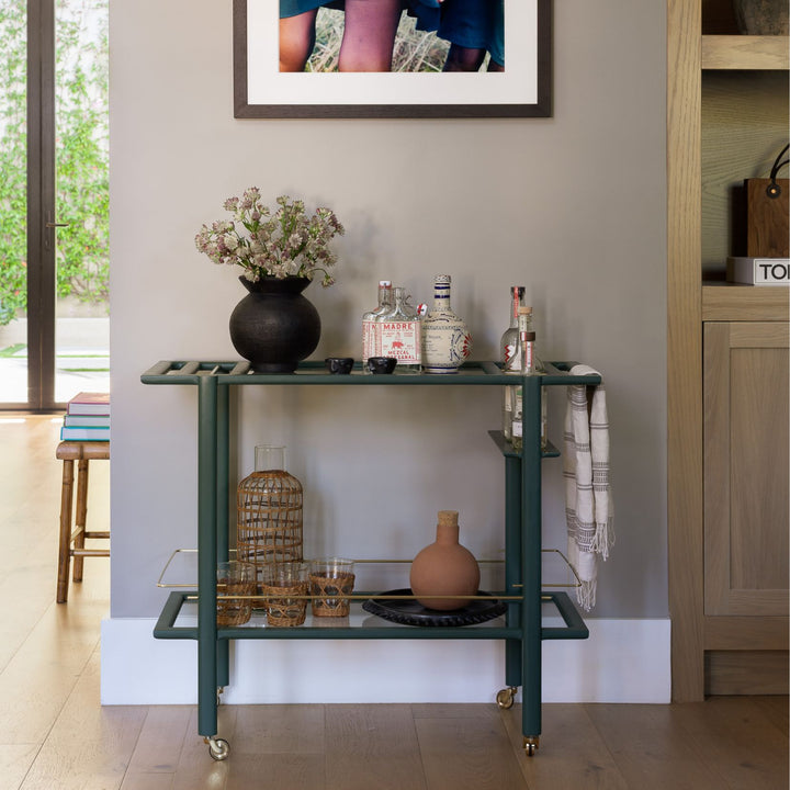 This bespoke BAR Cart from Earl Home is a custom hand made solid wood bar cart on wheels with exquisite hand-cut joinery, featuring two shelves: a robust tempered glass top and an elegant lower shelf made of clear or smoked tempered glass. This cart comes in walnut, white oak, ebonized oak, or lacquered in any pantone color. Brass, Copper and Aluminum are the metal types offered for detail.