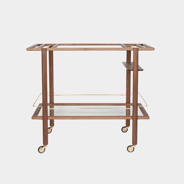 This bespoke BAR Cart from Earl Home is a custom hand made solid wood bar cart on wheels with exquisite hand-cut joinery, featuring two shelves: a robust tempered glass top and an elegant lower shelf made of clear or smoked tempered glass. This cart comes in walnut, white oak, ebonized oak, or lacquered in any pantone color. Brass, Copper and Aluminum are the metal types offered for detail.