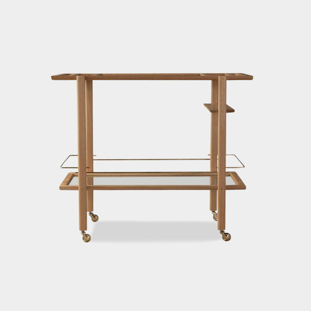 The BAR Cart from Earl Home is a solid wood bar cart on wheels with exquisite hand-cut joinery, featuring two shelves: a robust tempered glass top and an elegant lower shelf made of clear or smoked tempered glass. This cart comes in walnut, white oak, ebonized oak, or lacquered in any pantone color. Brass, Copper and Aluminum are the metal types offered for detail.