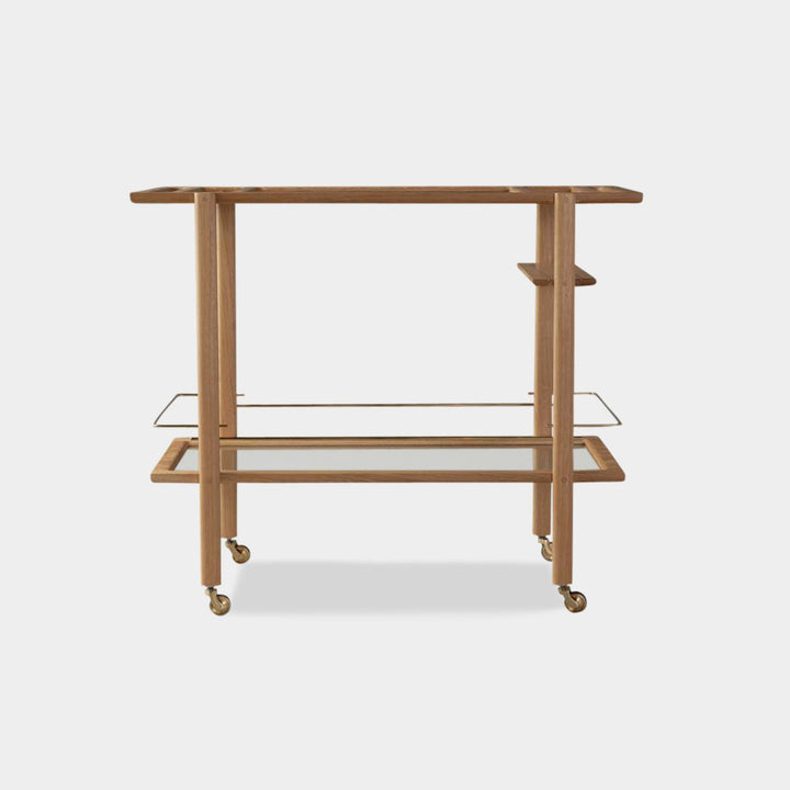 The BAR Cart from Earl Home is a solid wood bar cart on wheels with exquisite hand-cut joinery, featuring two shelves: a robust tempered glass top and an elegant lower shelf made of clear or smoked tempered glass. This cart comes in walnut, white oak, ebonized oak, or lacquered in any pantone color. Brass, Copper and Aluminum are the metal types offered for detail.