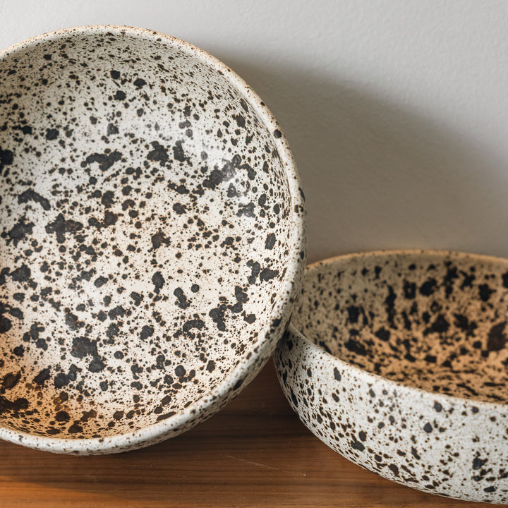 Two speckled ceramic bowls on a wooden surface with a neutral background