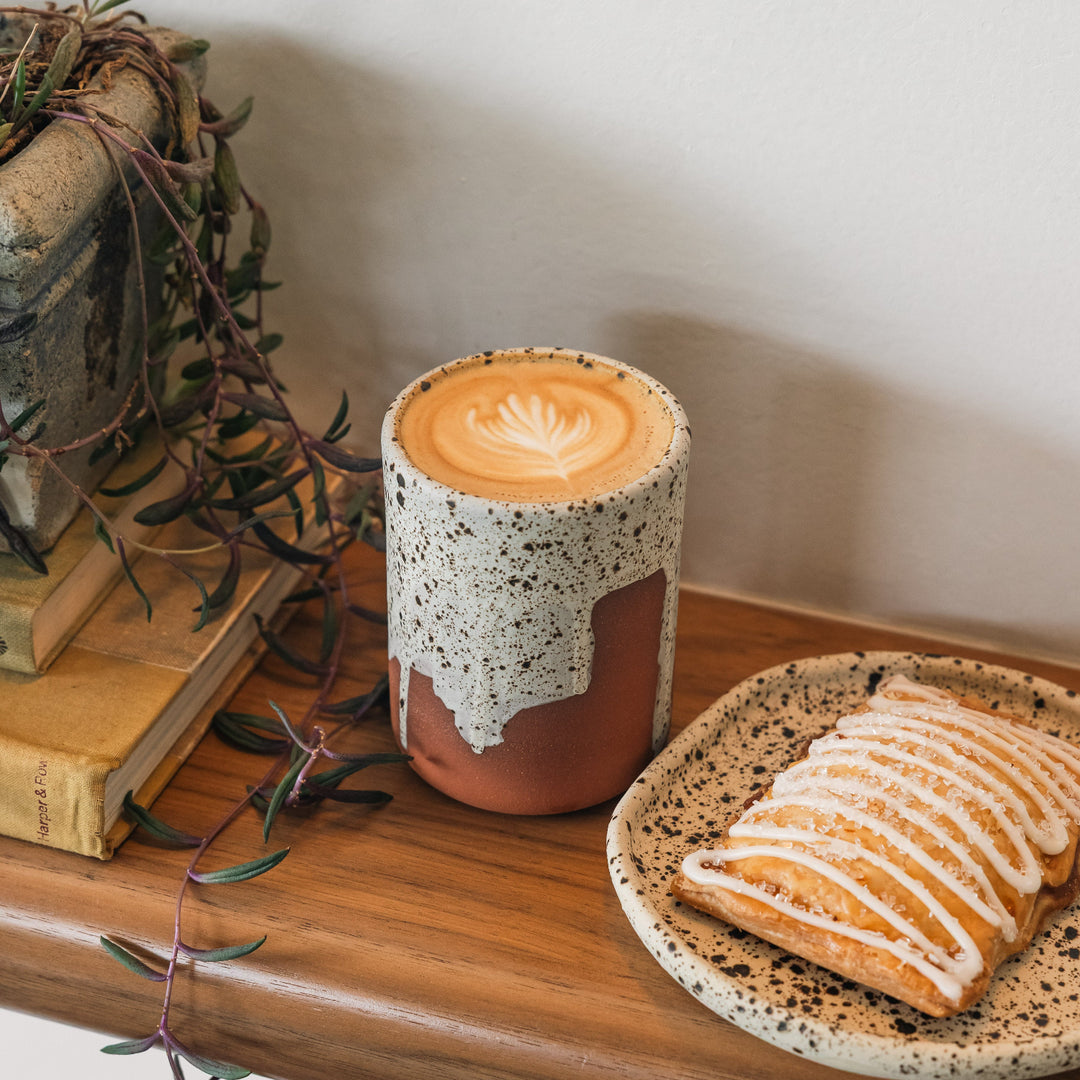 Cup of coffee with a decorative lid on a wooden surface with a pastry.