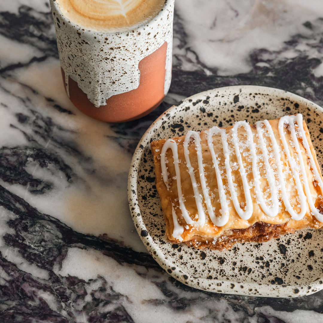 Cappuccino in a speckled cup with a pastry on a marble surface
