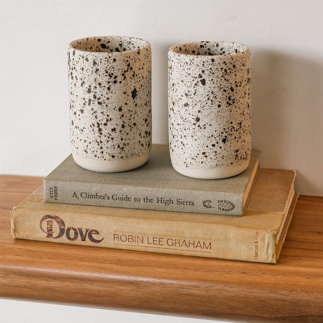 Two speckled ceramic cups on top of two books on a wooden surface.