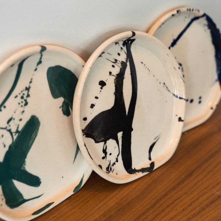 Three ceramic plates with black abstract designs on a wooden surface.