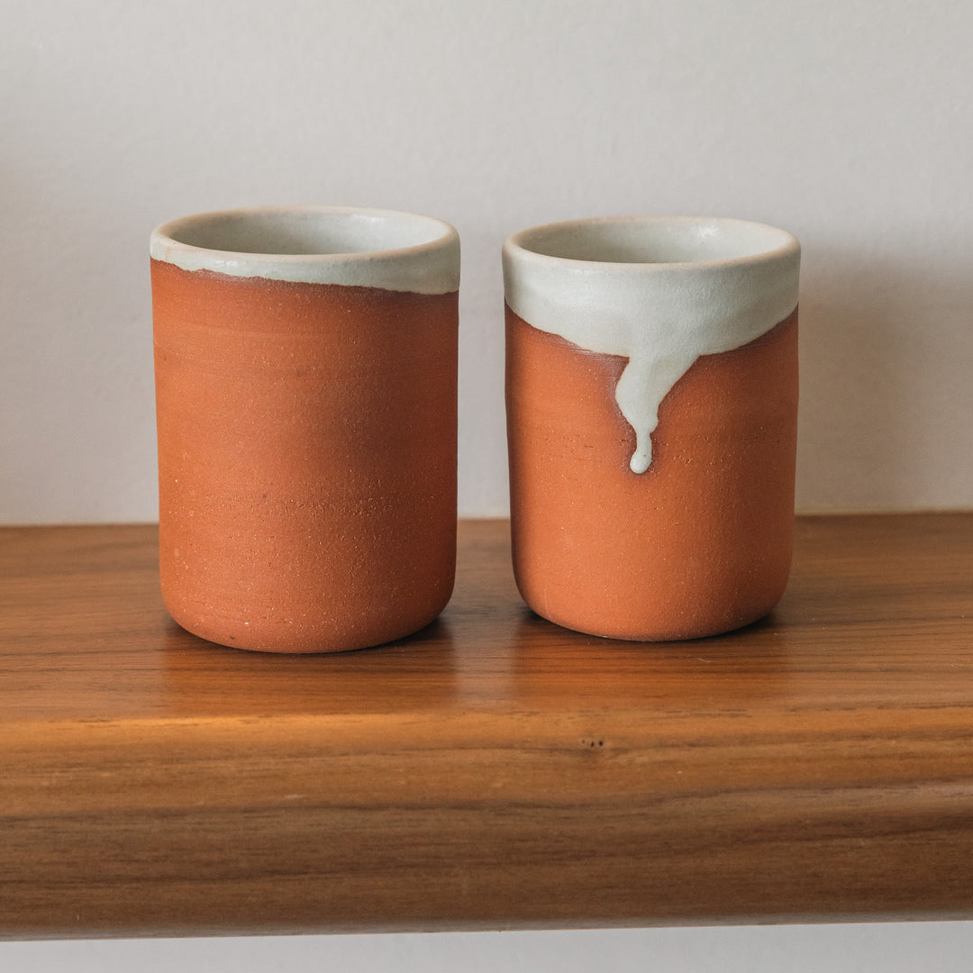 Two ceramic cups with terracotta clay and white glaze on a wooden surface.