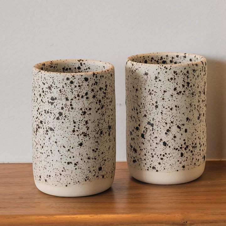Two ceramic cups and a unique vase on a wooden shelf against a plain wall.