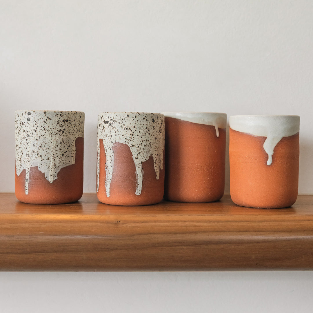 Four ceramic pots with speckled and glossy finishes on a wooden shelf.