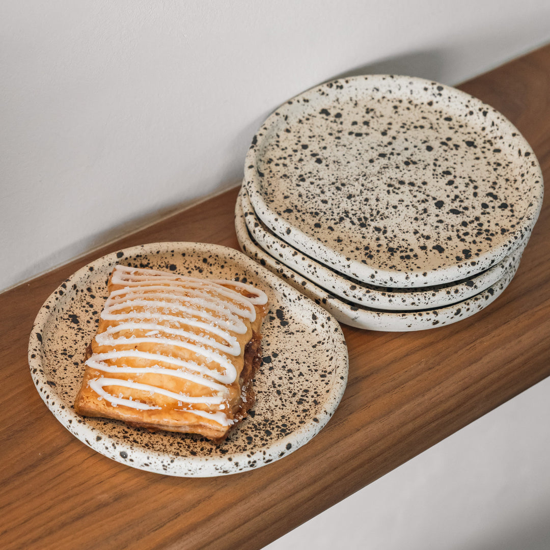 Speckled ceramic plates stacked on a wooden surface with a slice of cake or poptart.
