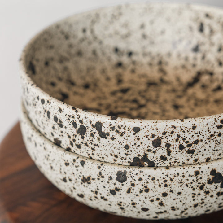 Speckled ceramic bowl on a wooden surface with a neutral background