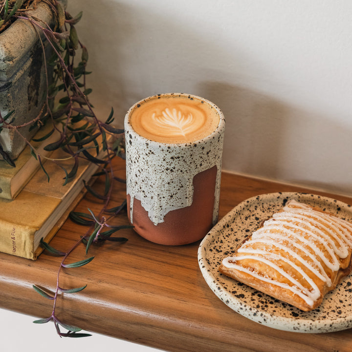 Cup of coffee with a decorative lid on a wooden surface with a pastry.