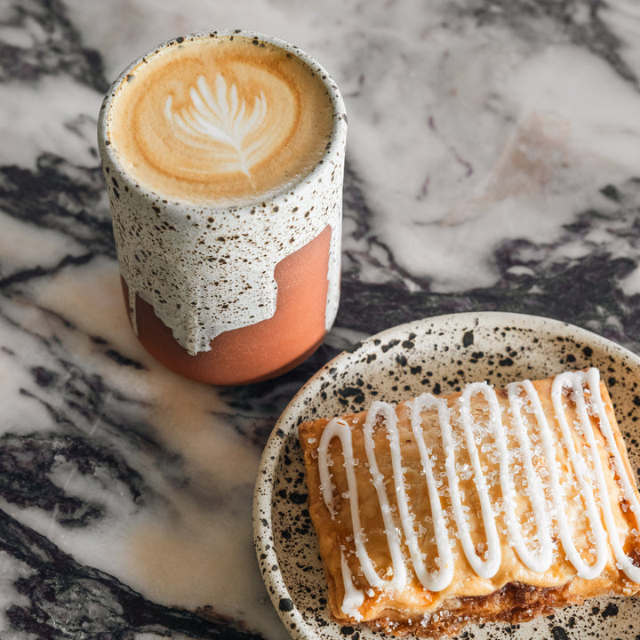 Cappuccino in a speckled cup with a pastry on a marble surface