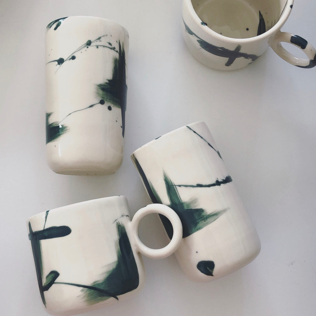 Four ceramic mugs with deep green abstract designs painted onto the cups.
