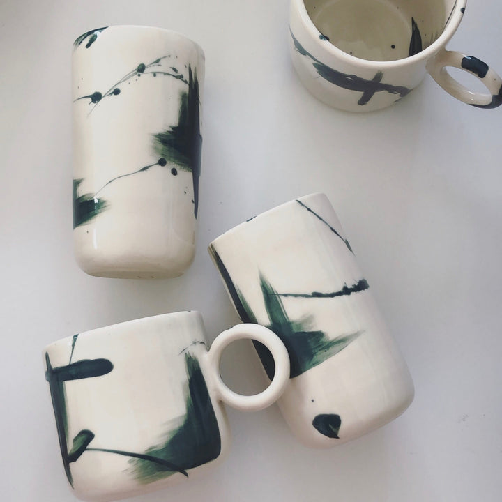 Four ceramic mugs with deep green abstract designs painted onto the cups.