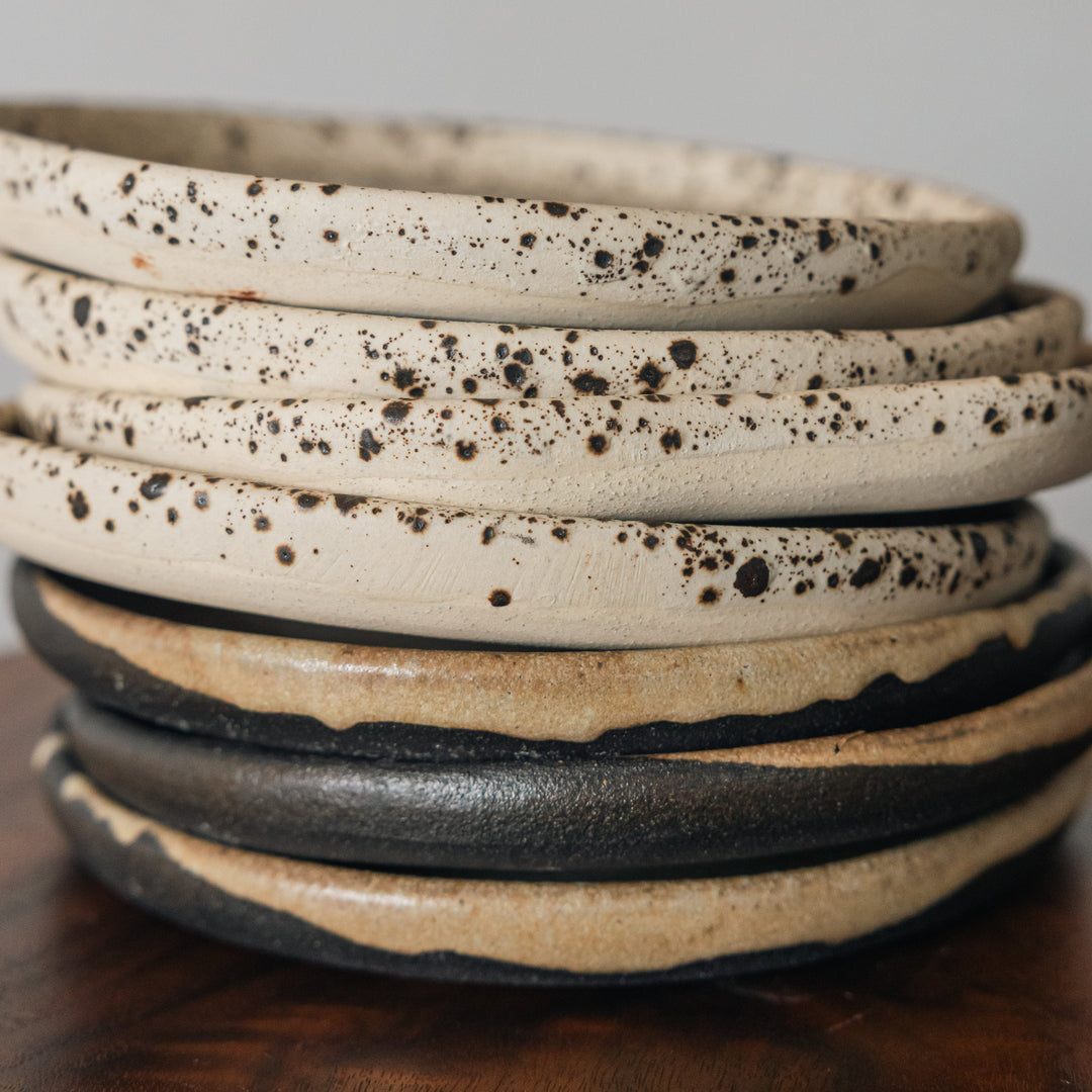 Stack of ceramic plates with speckled patterns on a wooden surface