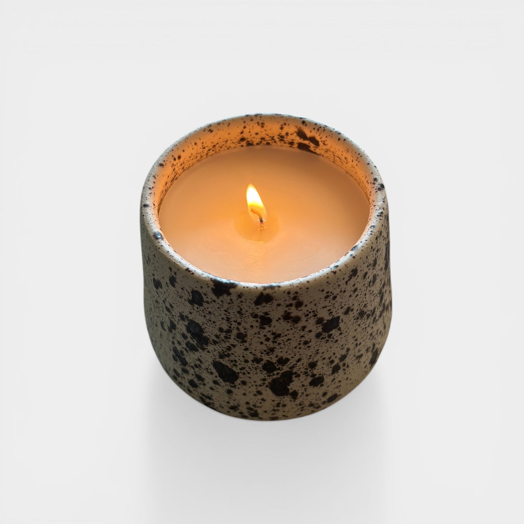 Speckled ceramic candle held by a hand with a plant in the background. Handmade in los Angeles, California. Made in America.