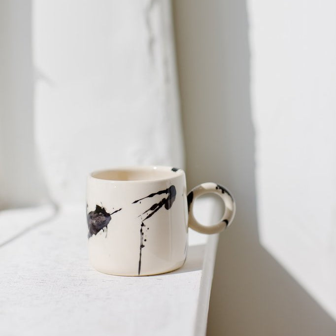 Ceramic mug with black abstract design on a white surface
Hand made pottery, hand thrown ceramic cup with terra cotta clay and cream splattered glaze, made in Los Angeles, California. Great for coffee, or tea. Microwave and dishwasher safe.