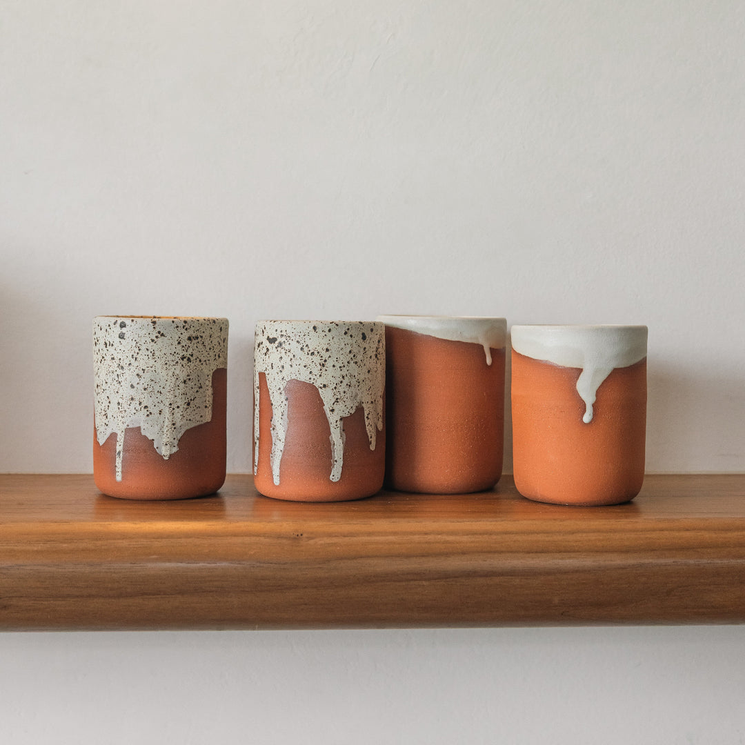 Four ceramic jars with a unique glaze pattern on a wooden shelf against a plain background