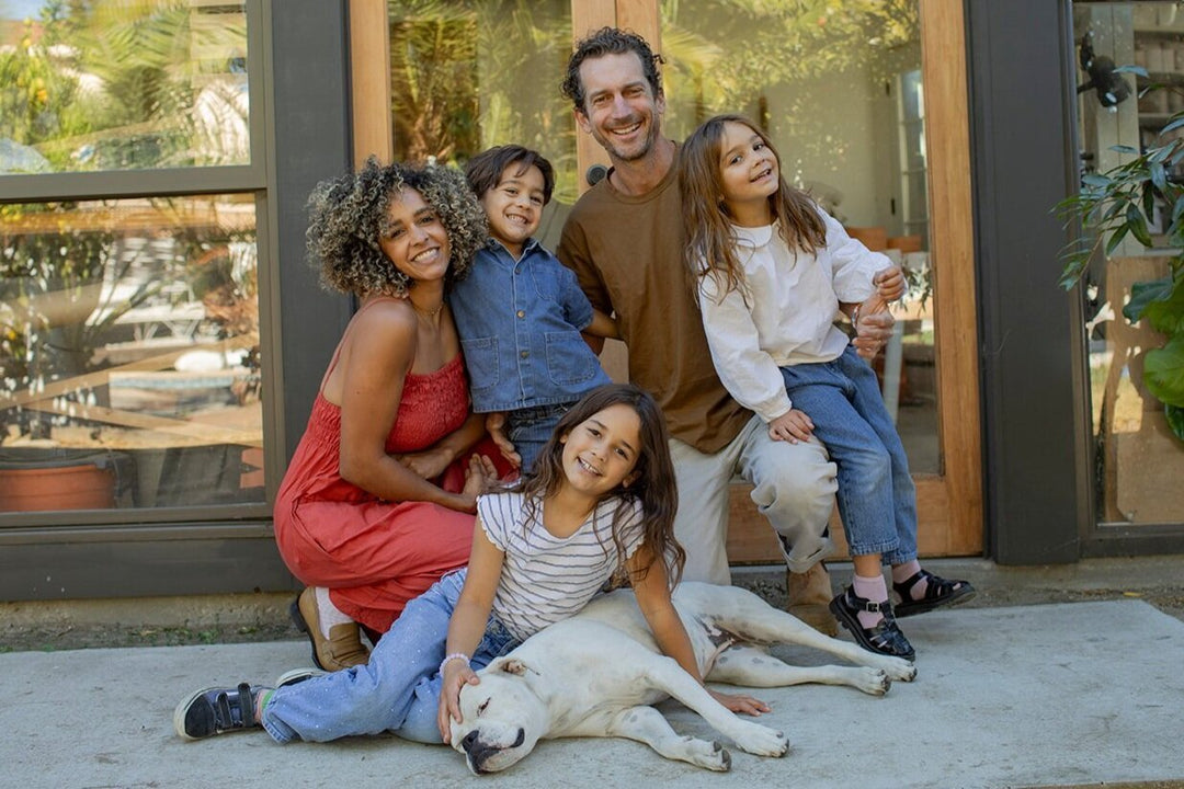 Family with three children and a dog pose happily in front of a house.