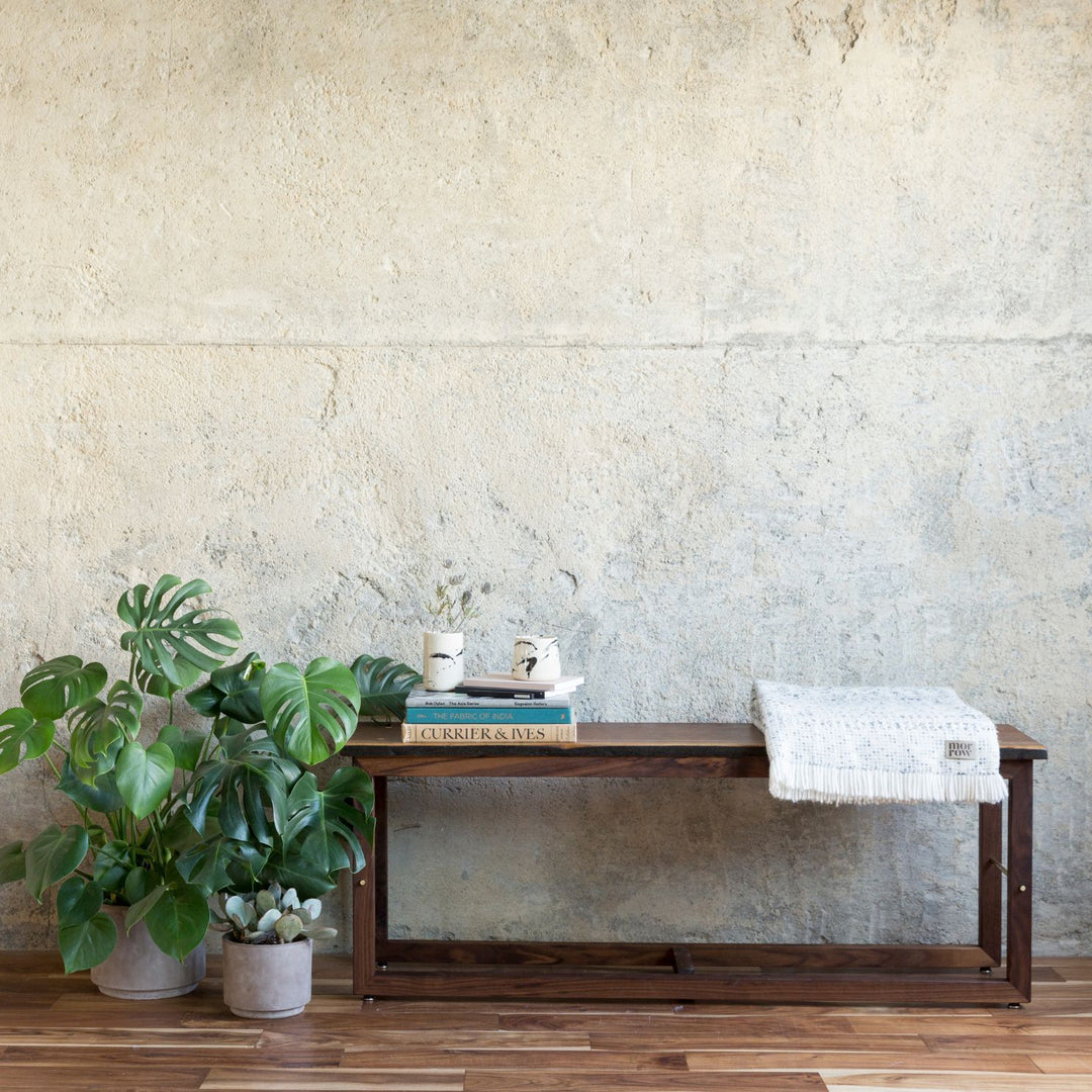 The Earl Home Walnut HAROLD Bench is a handcrafted masterpiece with a simple rectangular design and an open frame, featuring elegant walnut wood and brass detailing.