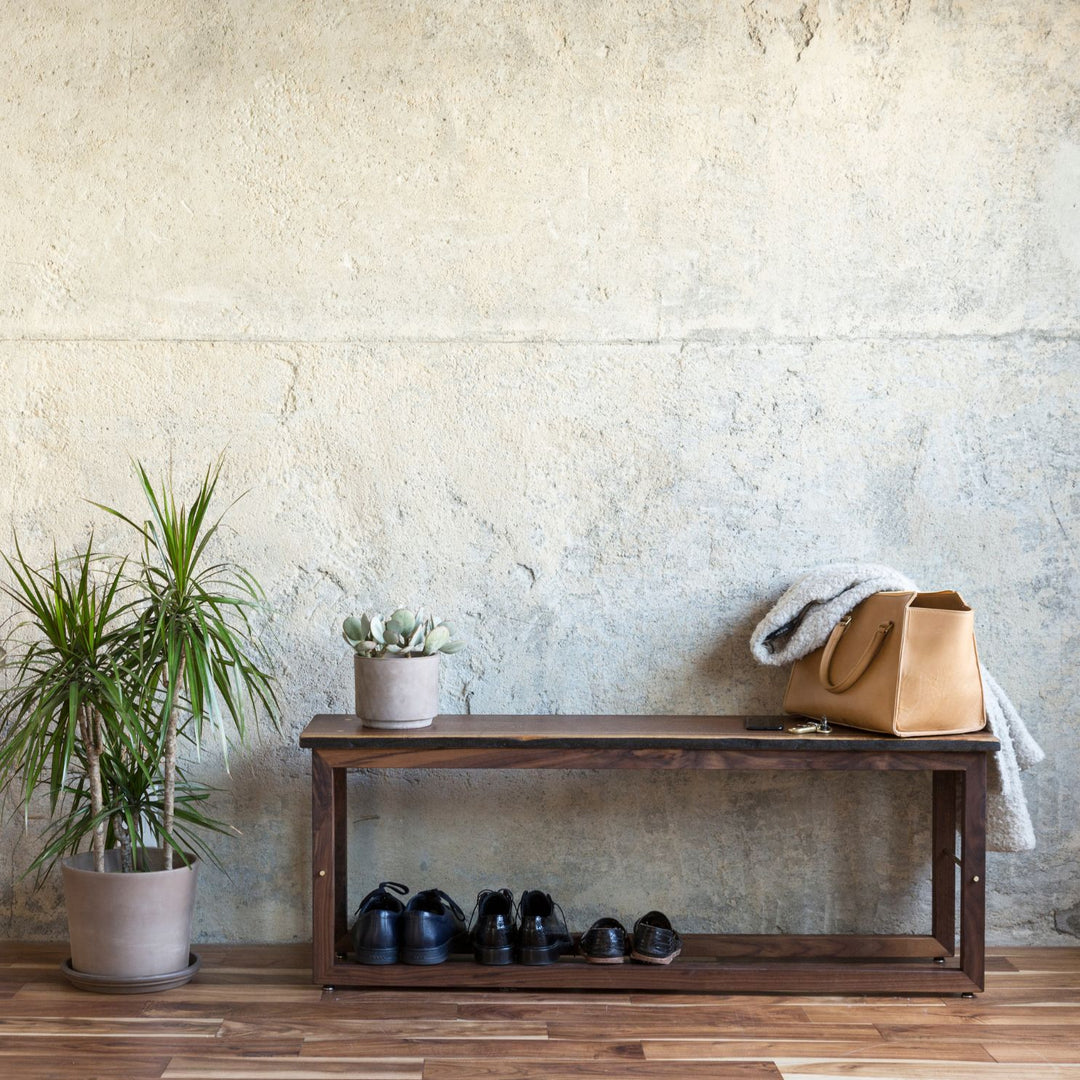 The Earl Home Walnut HAROLD Bench is a handcrafted masterpiece with a simple rectangular design and an open frame, featuring elegant walnut wood and brass detailing.