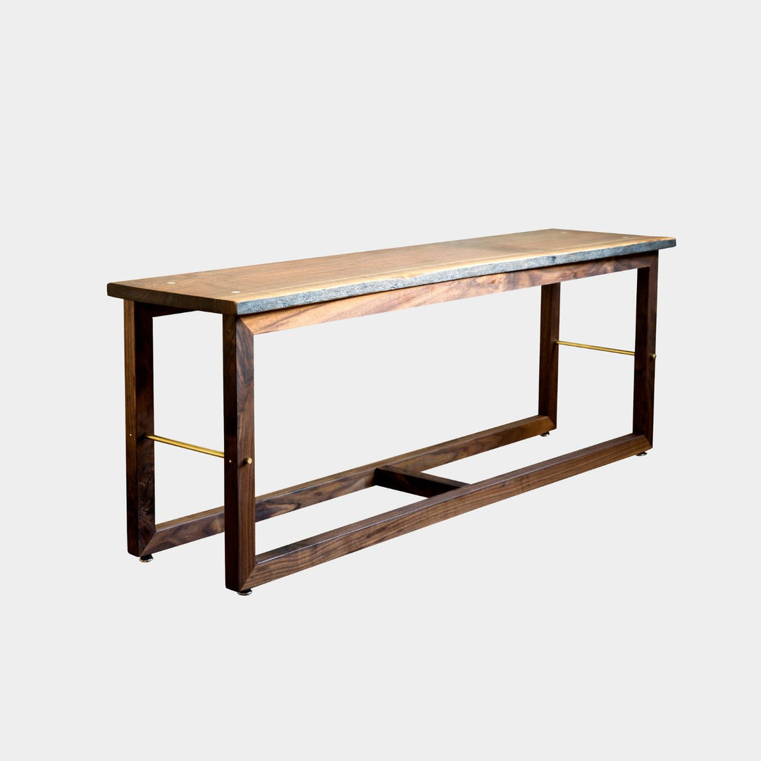 The Earl Home Walnut HAROLD Bench is a handcrafted masterpiece with a simple rectangular design and an open frame, featuring elegant walnut wood and brass detailing.