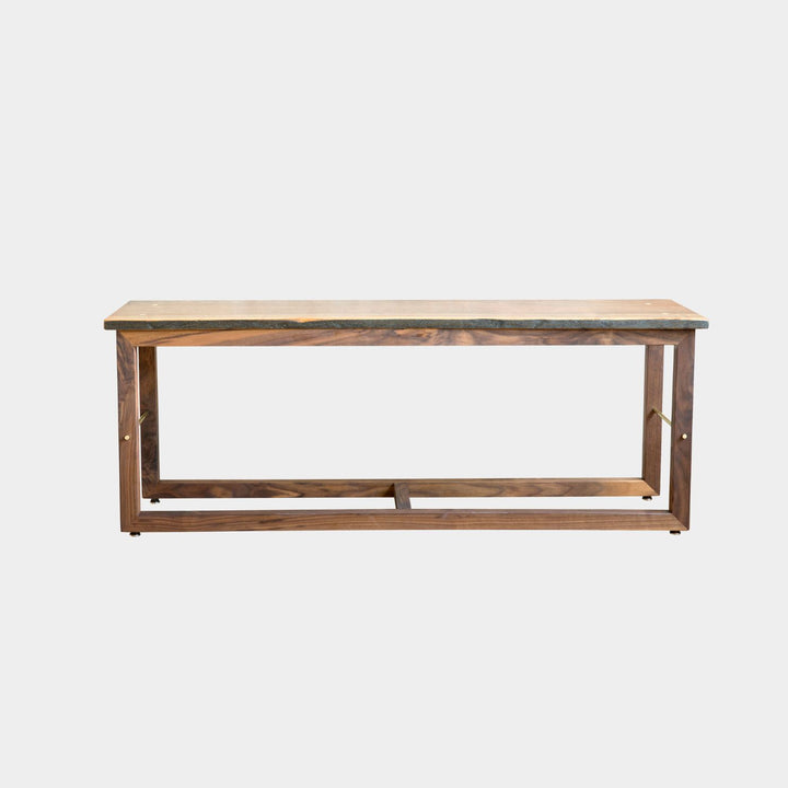 The Earl Home Walnut HAROLD Bench is a handcrafted masterpiece with a simple rectangular design and an open frame, featuring elegant walnut wood and brass detailing.