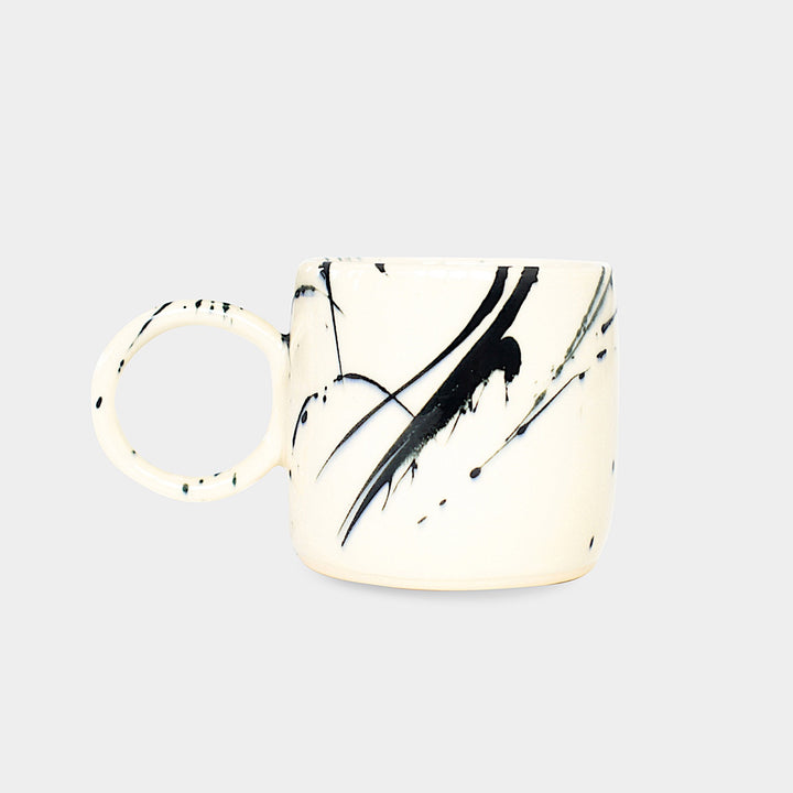 Earl Home's CIRCLE Mug is a hand-thrown white ceramic mug with black brush stroke splatters and a round handle.