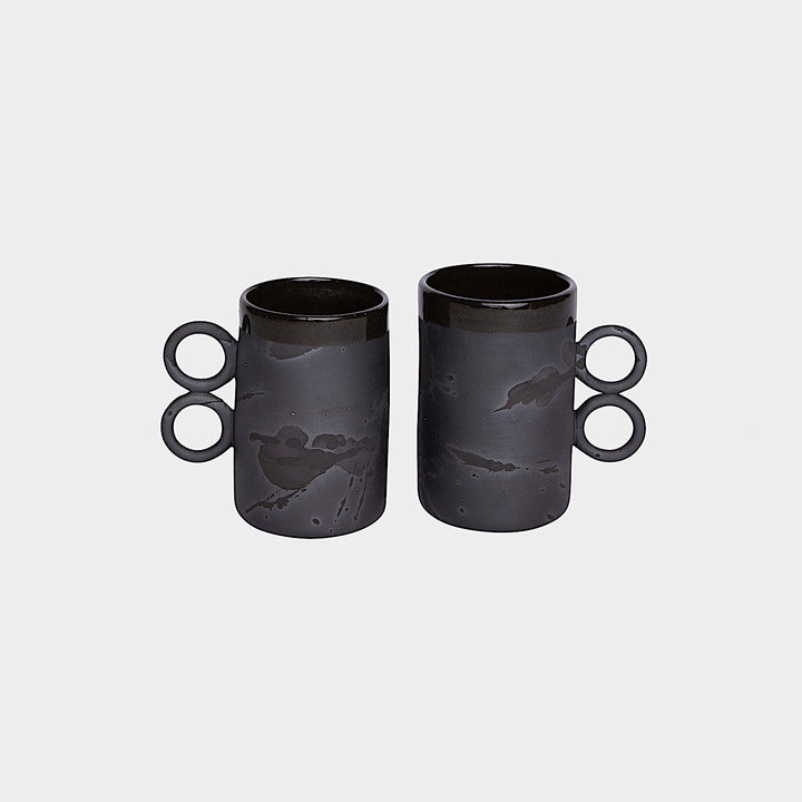 The Earl Home DOUBLE Handle Mug set includes two brown ceramic mugs, each featuring a unique round handle and white abstract patterns. Hand-thrown for artisanal charm, these mugs are perfect for those who appreciate the delicate artistry of ceramic craftsmanship.