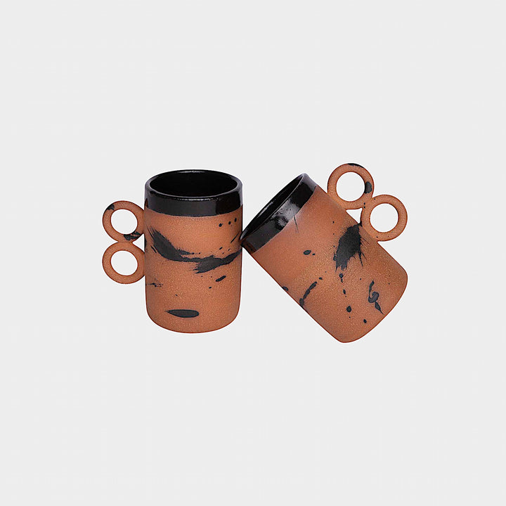 The Earl Home DOUBLE Handle Mug set includes two brown ceramic mugs, each featuring a unique round handle and white abstract patterns. Hand-thrown for artisanal charm, these mugs are perfect for those who appreciate the delicate artistry of ceramic craftsmanship.