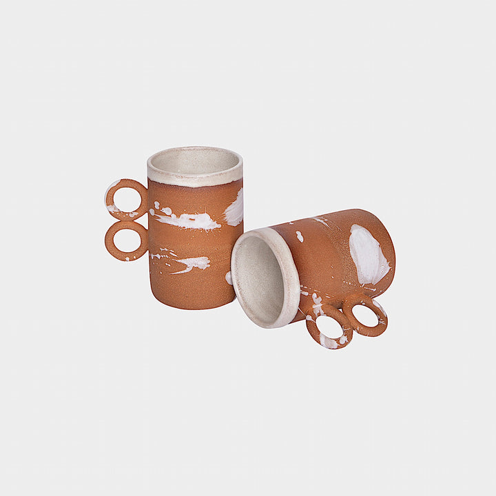 The Earl Home DOUBLE Handle Mug set includes two brown ceramic mugs, each featuring a unique round handle and white abstract patterns. Hand-thrown for artisanal charm, these mugs are perfect for those who appreciate the delicate artistry of ceramic craftsmanship.