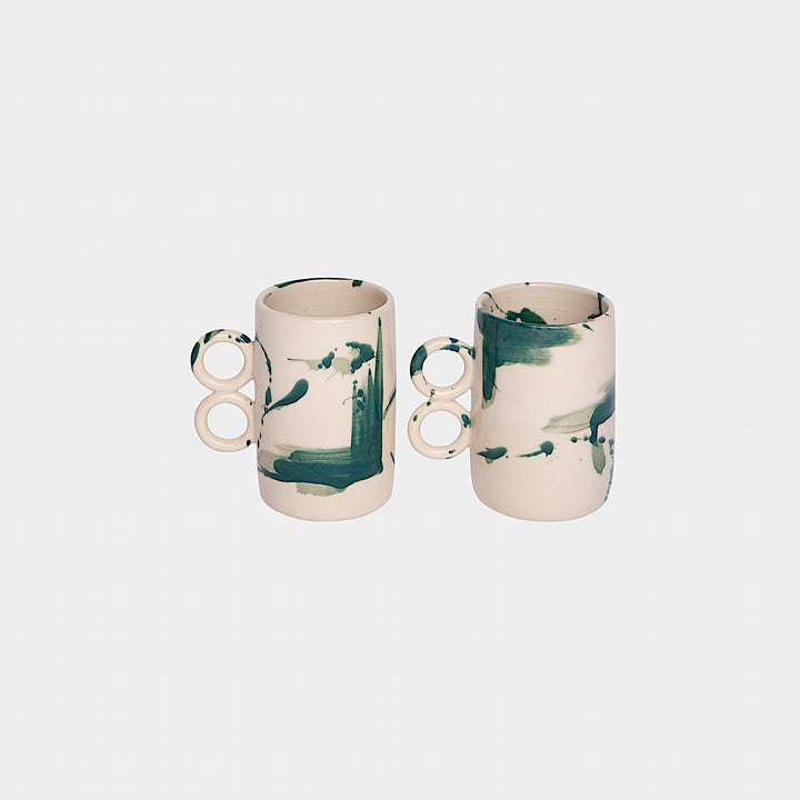 The Earl Home DOUBLE Handle Mug set includes two brown ceramic mugs, each featuring a unique round handle and white abstract patterns. Hand-thrown for artisanal charm, these mugs are perfect for those who appreciate the delicate artistry of ceramic craftsmanship.