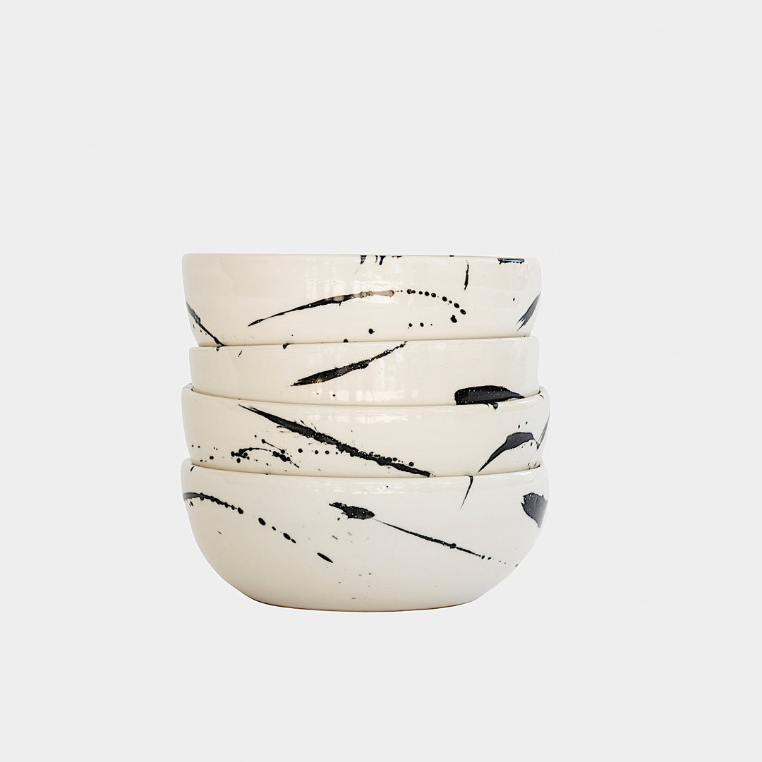 The Earl Home PASTA Bowl set includes four stylish white ceramic bowls featuring black abstract splatter designs. Each unique, hand-thrown piece is dishwasher safe, perfect for adding a distinct touch to your kitchen collection.