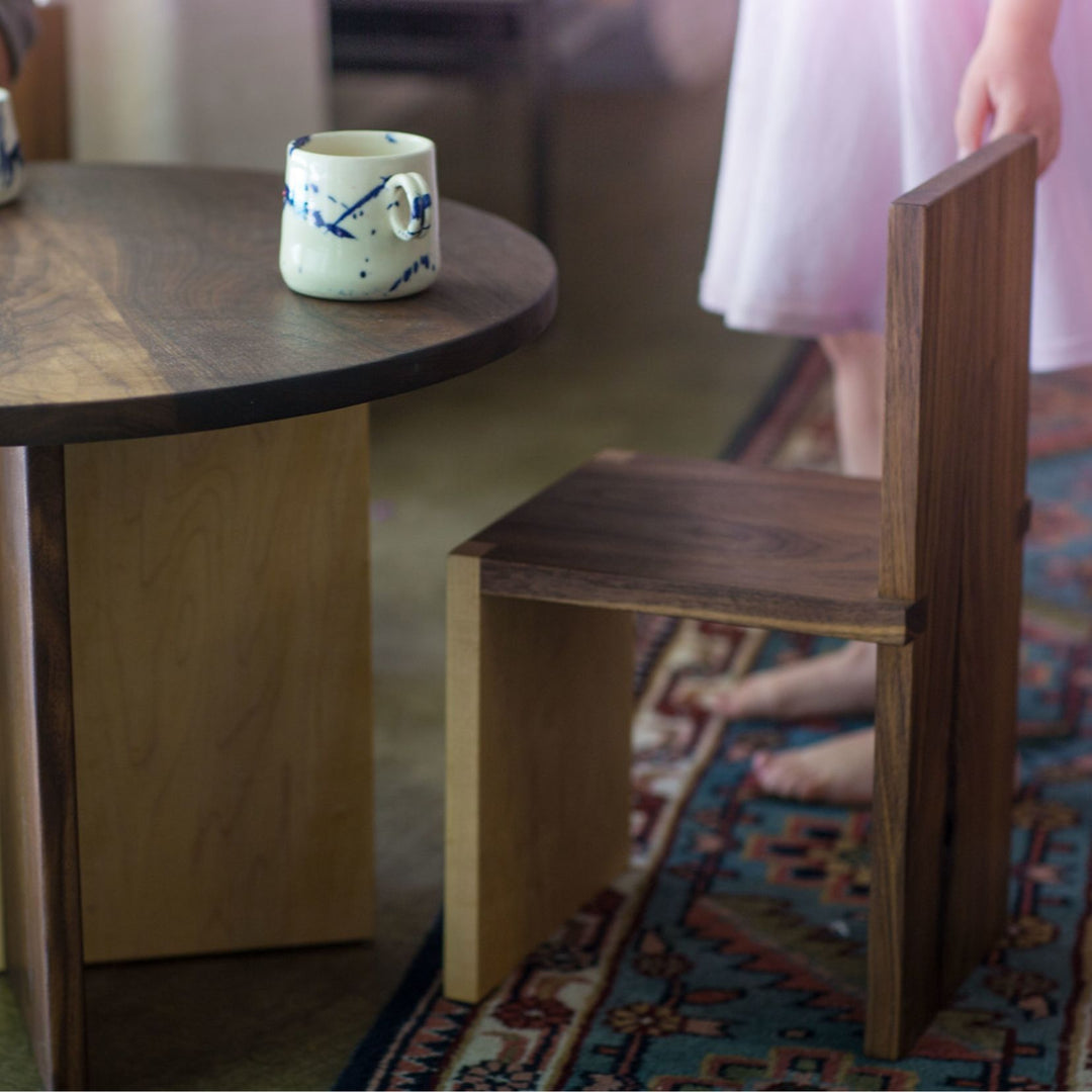 The Earl Home KIDS Set, featuring a custom, round wooden table made from sustainably sourced American hardwood. Two rectangular chairs are ideally positioned on opposite sides for a kid's table setup. Walnut mixed with maple, solid walnut, solid white oak, ebonized oak are all options for this custom made to order set.